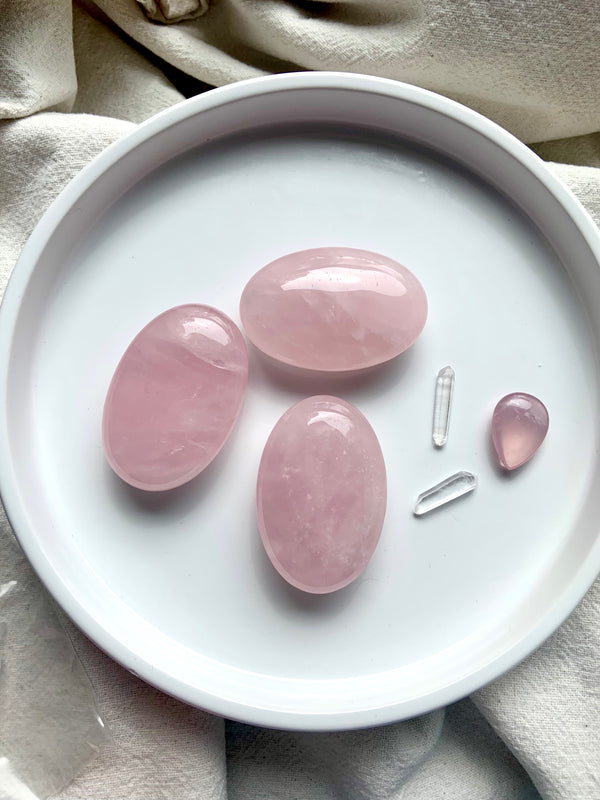 Three beautiful translucent pink Rose Quartz Palm Stones shown on a plate with a few other smaller crystals.