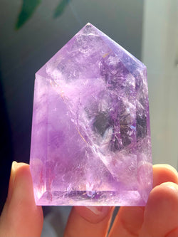 A gorgeous purple Amethyst Point held up to allow natural light to illuminate the crystal