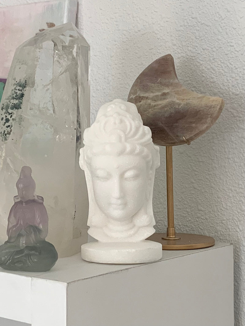 White Jade Quan Yin Statue shown on a shelf with some larger crystals and another Quan Yin figurine in the picture.