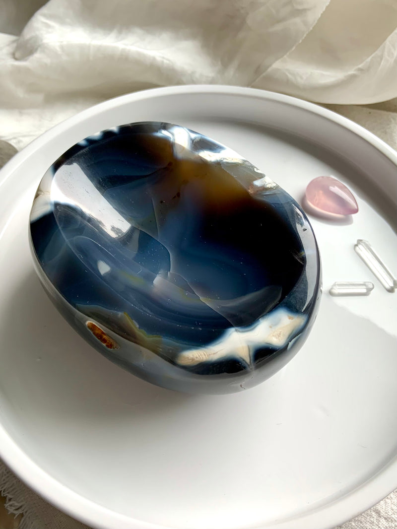 Large, hand carved Orca Agate Offering Bowl shown on a white plate with some small crystals in the background