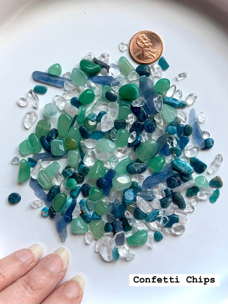 Showing the Mermaid Crystal Confetti Mix spread on a white plate with a penny and my hand for scale