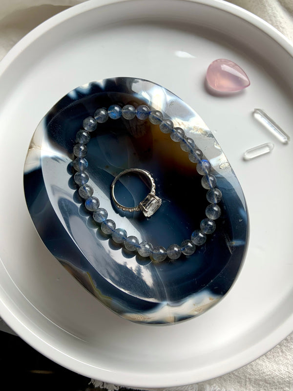 Large, hand carved Orca Agate Offering Bowl shown holding a ring and a bracelet, set on a white plate with some small crystals in the background