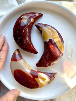 Palm sized, hand carved Mookaite Jasper Crescent Moons shown on a white background with my hand for scale. Choose your favorite!